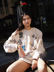 Woman sitting outdoors wearing a white sweatshirt with colorful designs.