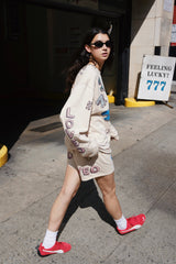 Person walking on a city street wearing a beige outfit with text and red shoes.