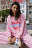 Person wearing a pink sweatshirt with 'Grateful For Today' text and hearts, sitting on a street corner.